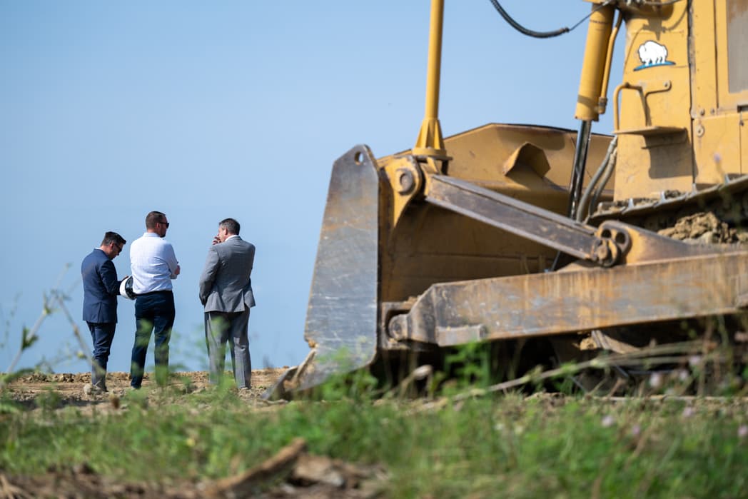 Three executives in suits conversing at construction site next to heavy equipment — Cincinnati event photographer K Dalton