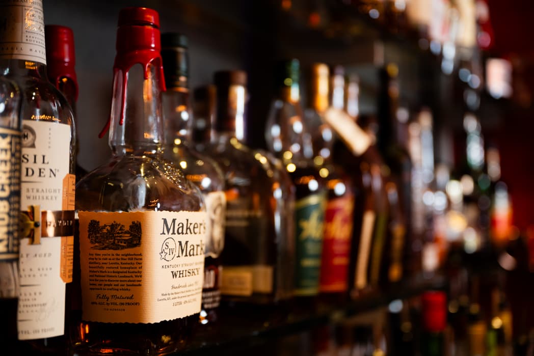 Bourbon and whiskey bottles lined up on bar shelf at corporate cocktail event — Cincinnati event photographer K Dalton