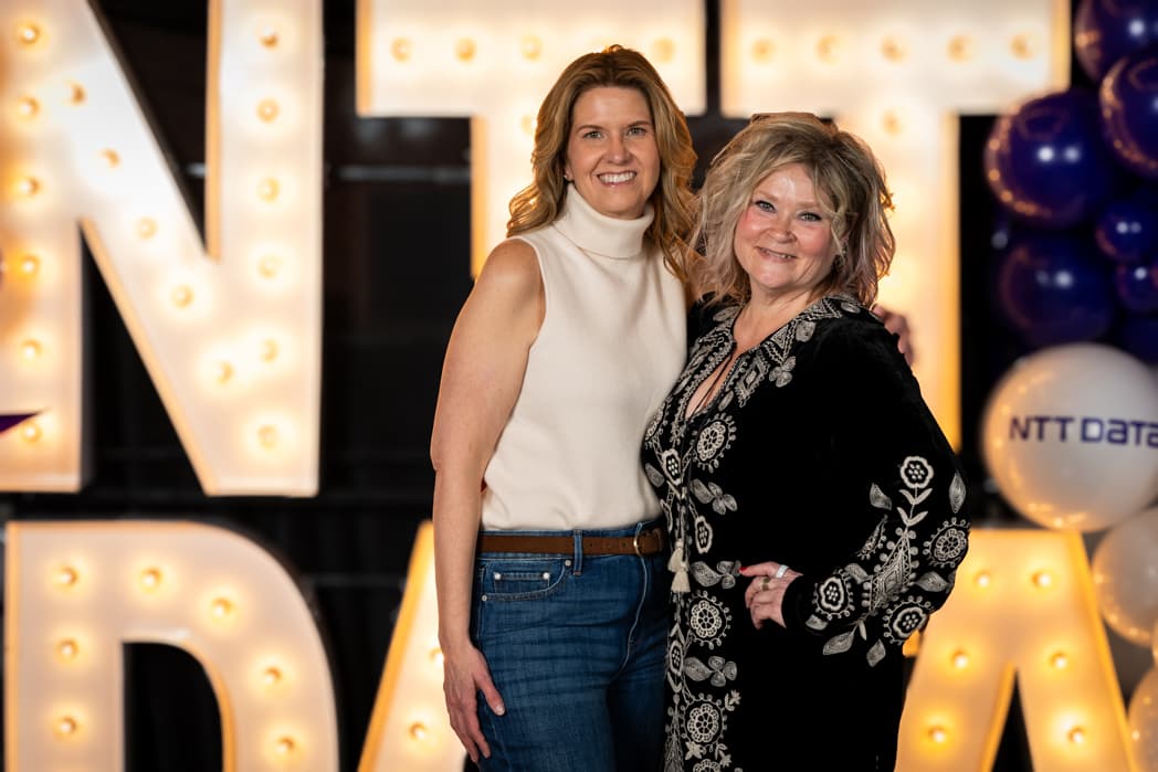 Two women posing together in front of illuminated NTT Data marquee letters at corporate gala — Cincinnati event photographer K Dalton