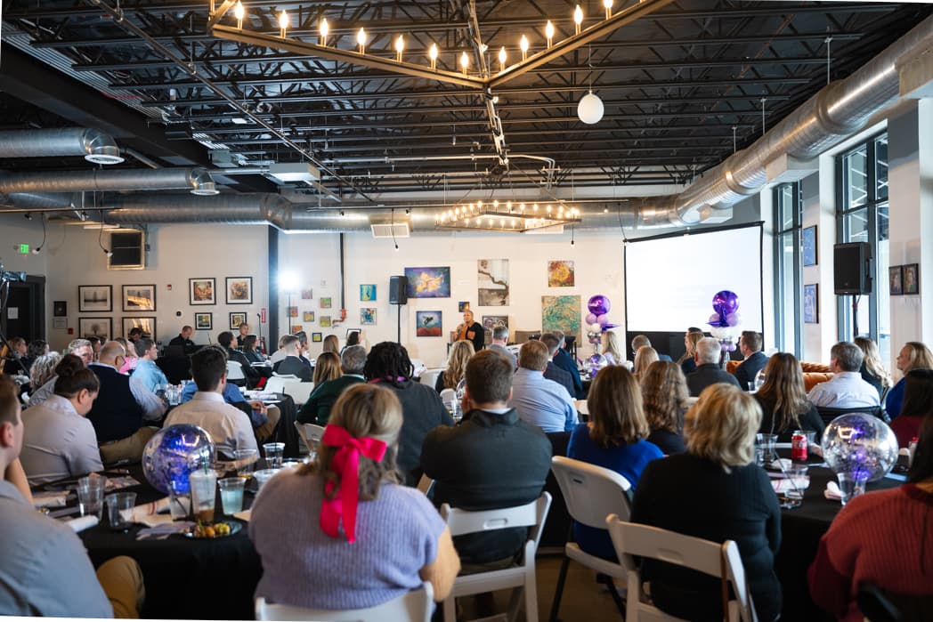 Full conference room of professionals seated at round tables watching keynote presentation at corporate event — Cincinnati event photographer K Dalton