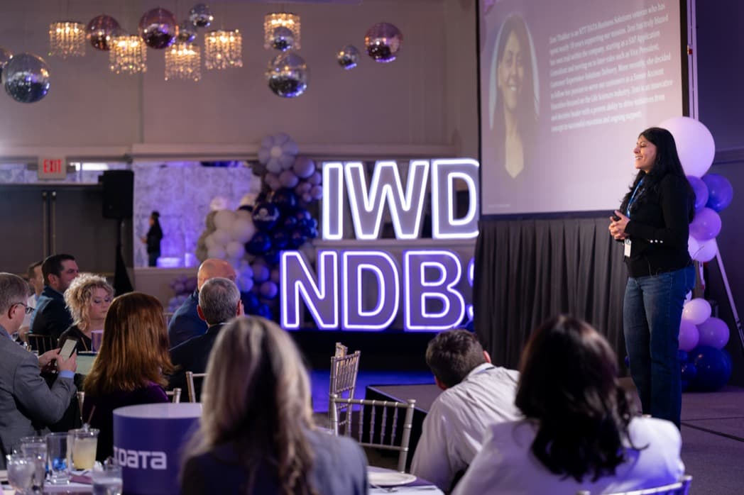 Speaker presenting on stage at corporate conference with illuminated signage and balloon decor — Cincinnati event photographer K Dalton